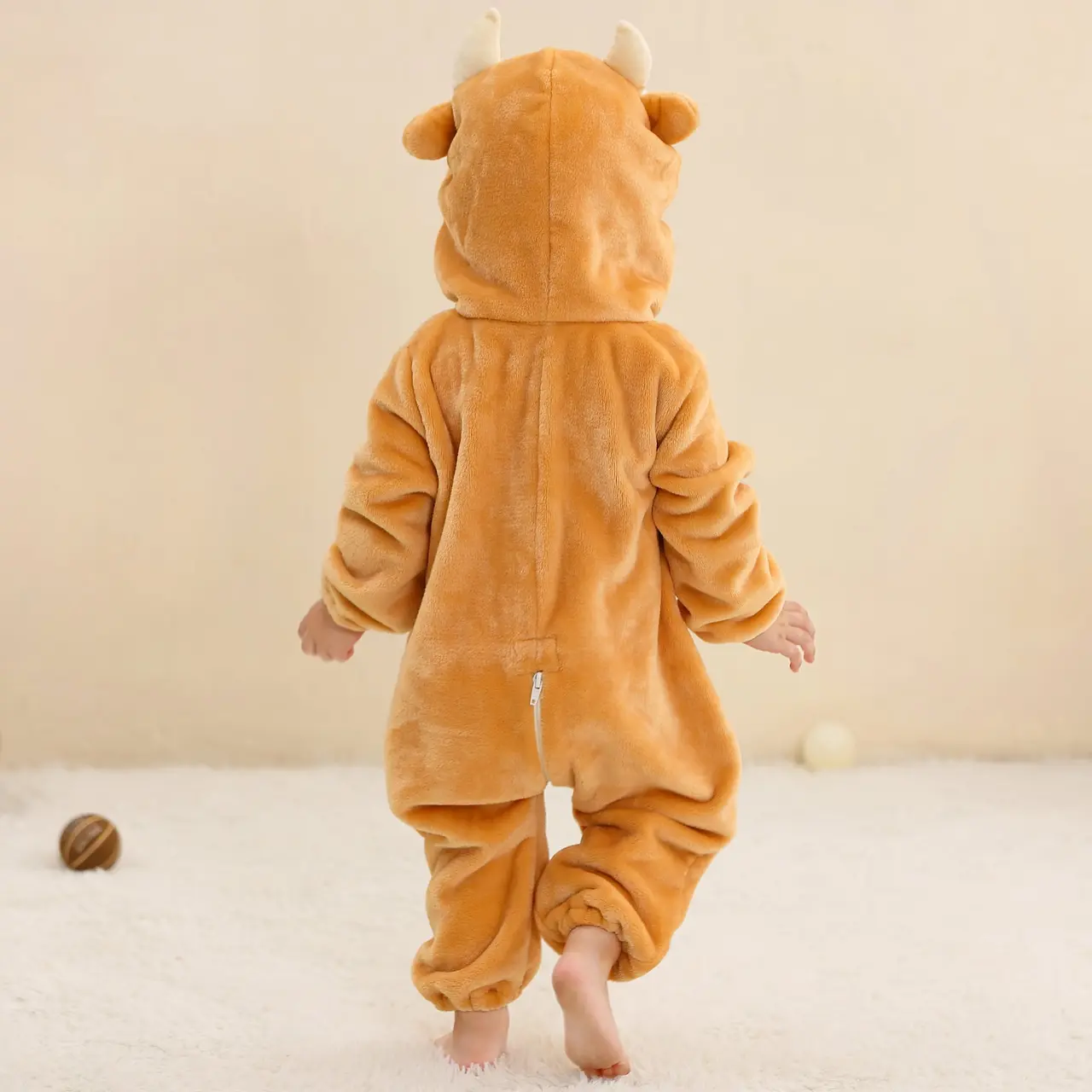 Et blødt og behageligt tyrekostume til børn i brun flannel. Dragten har en hvid mave, en sød hætte med horn og ører samt en lille hale bagpå, hvilket gør den perfekt til både leg og fastelavn.