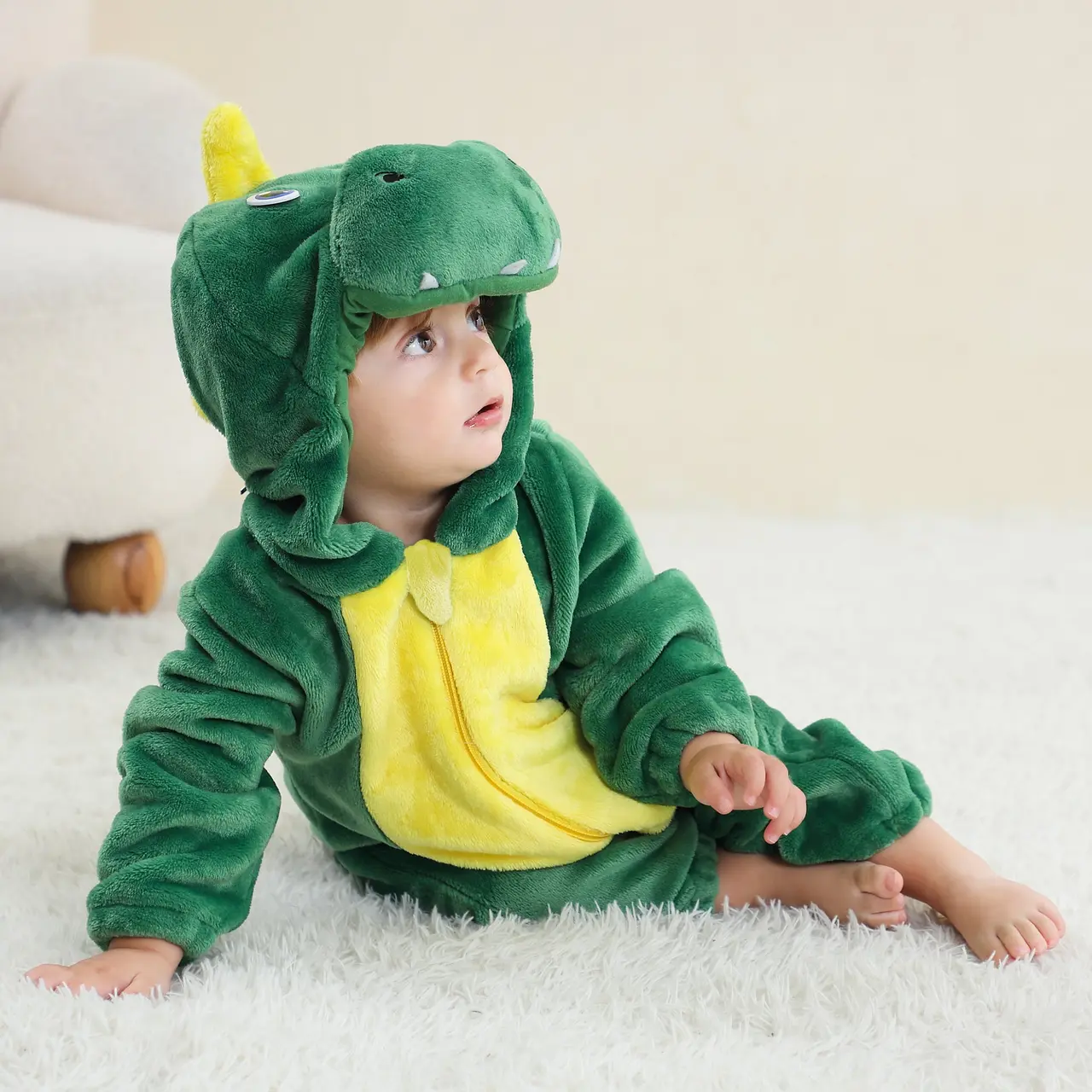 Et blødt og nuttet grønt T-Rex kostume til børn, lavet af behageligt flannelmateriale. Dragten har en sjov hætte med dinosauransigt og hvide tænder samt en lille hale bagpå.