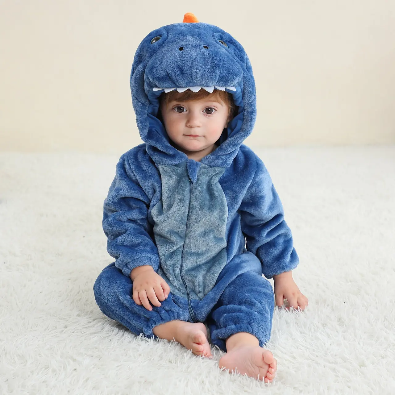 Billedet viser et charmerende og blødt blåt T-Rex kostume til børn, set fra siden. Dragten er lavet af vamset flannel med en hvid mave, takker langs ryggen og en matchende hætte med et sødt dinosauransigt, hvilket gør den ideel til både leg og fastelavn.