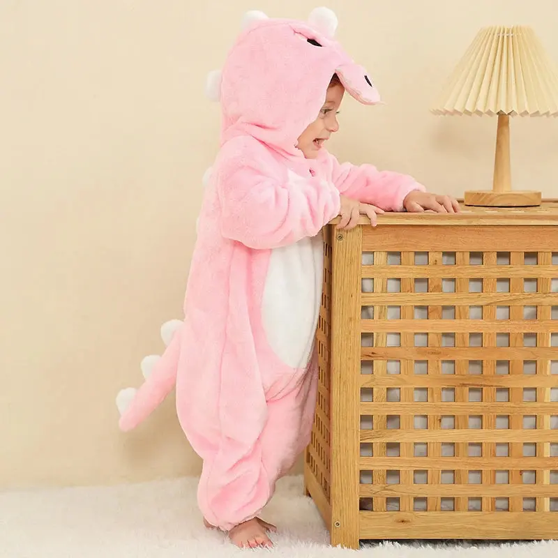 Dette billede viser et nuttet og blødt lyserødt T-Rex kostume til børn, fremstillet i behageligt flannelmateriale med et detaljeret skælmønster. Dragten har en fastgjort hætte med hvide tænder og øjne samt en polstret hale bagpå, hvilket gør den perfekt til både fastelavn og sjov leg.