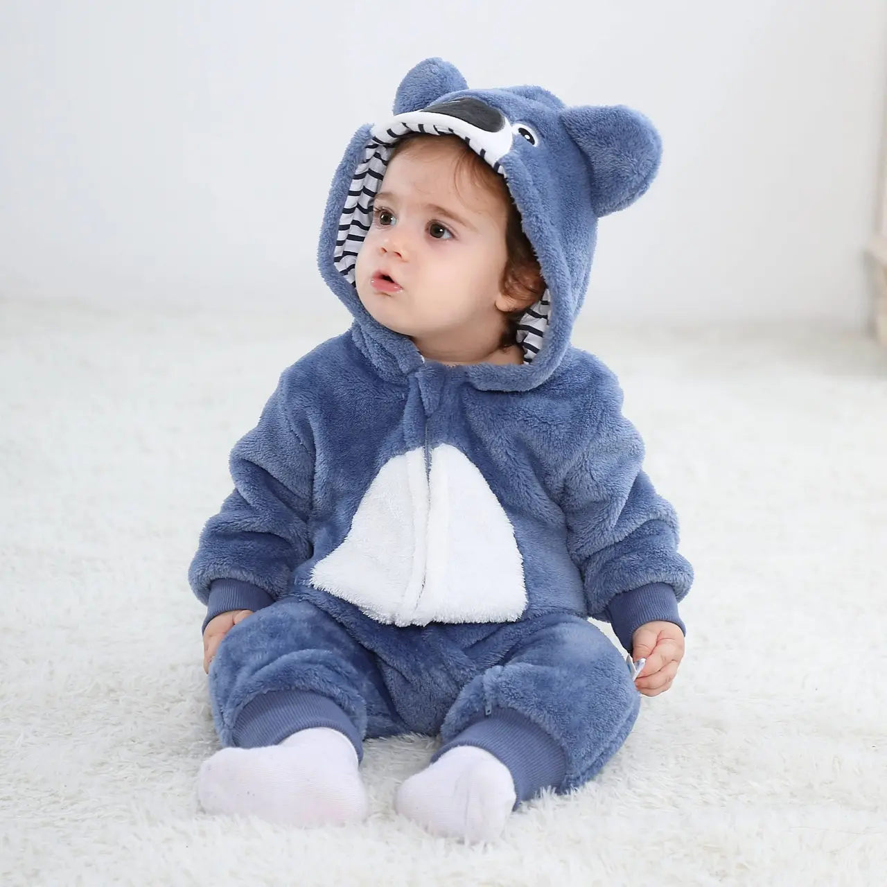 Dette billede viser et charmerende lyseblåt koala-kostume til børn, set bagfra. Dragten er lavet af blødt flannelmateriale og har en sød lille hale samt en matchende hætte med store, mørke koala-ører, hvilket gør den perfekt til både leg og fastelavn.