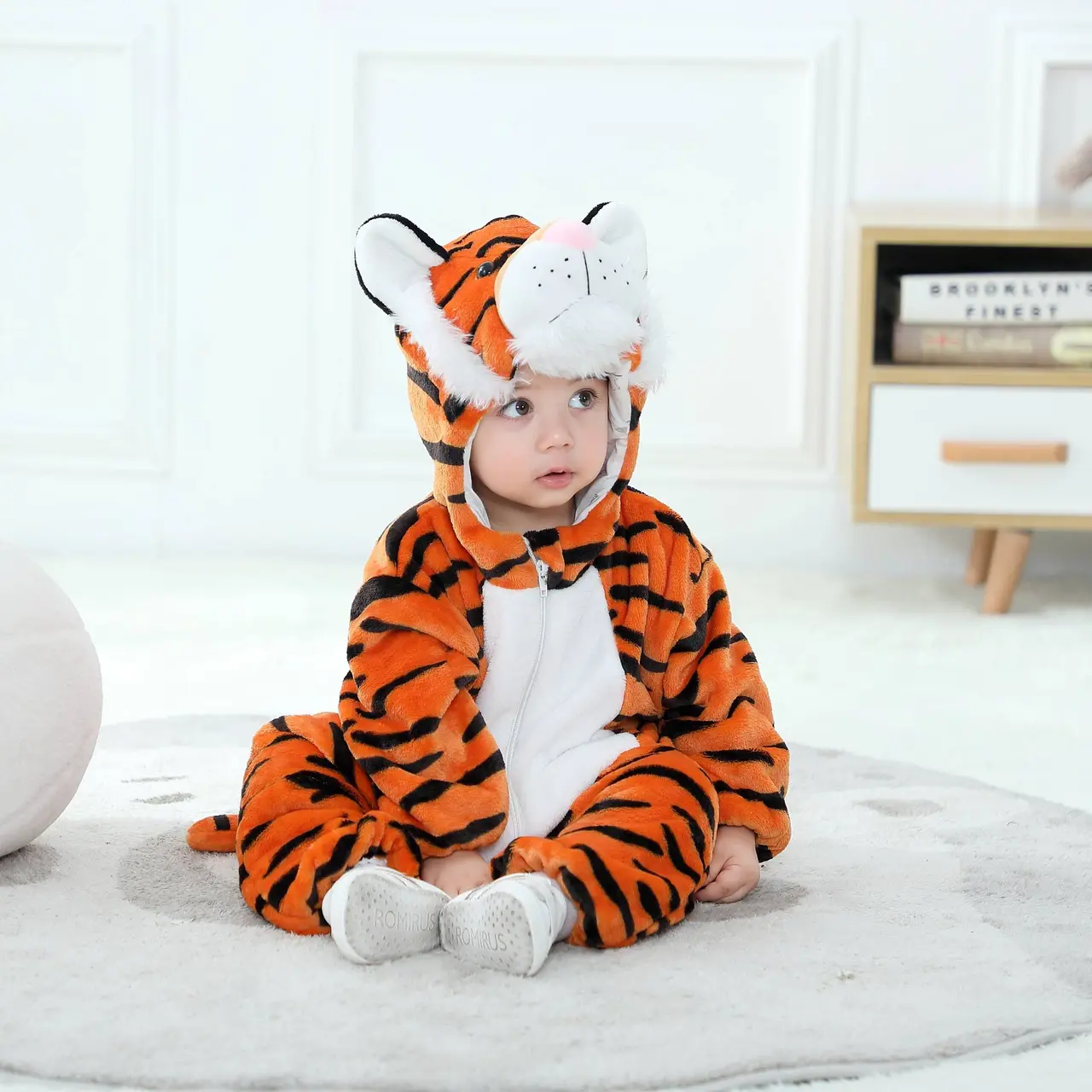 Et nuttet og blødt orange tigerkostume til børn med sorte striber, hvid mave og en matchende hætte med små ører. Dragten er lavet af behageligt flannelmateriale og har en praktisk lynlås foran, der gør den ideel til både leg og fastelavn.