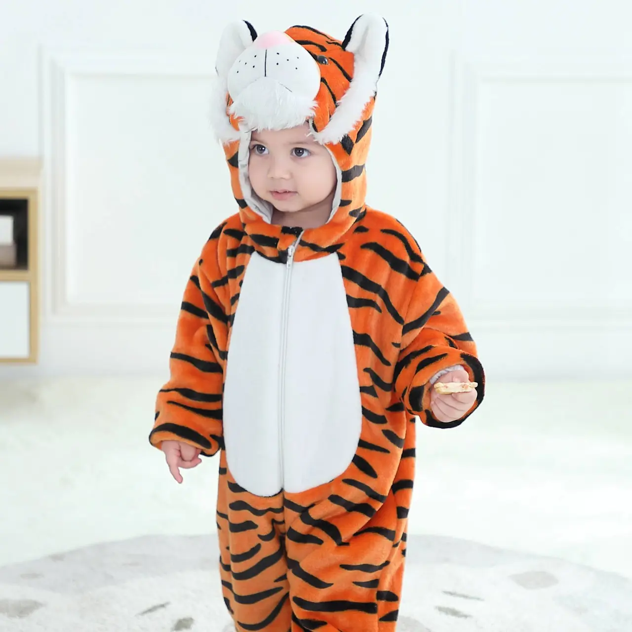 Et nuttet og blødt orange tigerkostume til børn, lavet af behageligt flannelmateriale med sorte striber. Dragten har en hvid mave, en hætte med små ører og et detaljeret tigeransigt, samt en lille hale bagpå, perfekt til leg eller fastelavn.